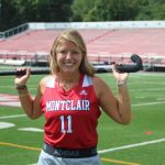 photo of Evyn Stewart standing on the field, empty stadium seats are behind her. she holds her field hockey stick over both sholders