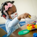 A child places toys into a container, indicating that she’s heard a beep through her headphones during a hearing exam.