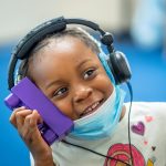 A student in Newark holds a block to her ear while listening for a “beep” through headphones.