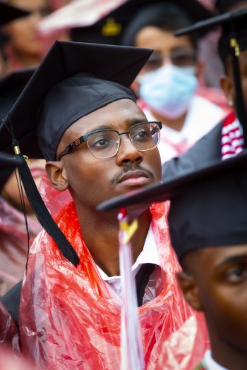 photo of student Dior Cleaves in the crowd of graduates. He's wearing a cap and gown and looking forward in the direction of the stage.