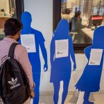 "A man stands in front of blue cardboard cutouts that represent survivors of human trafficking."