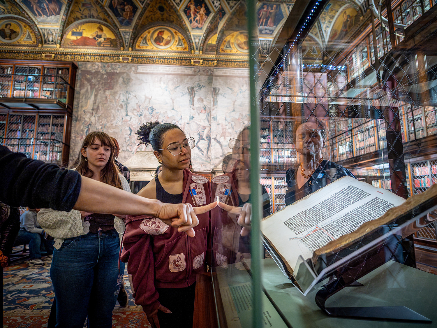 a tour guide points on a glass case which holds an Gutenberg Bible as students look on