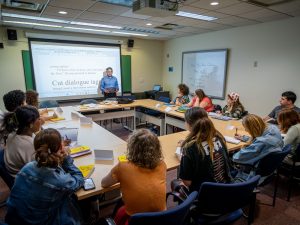 "David Galef stands at the front of a classroom, addressing students."