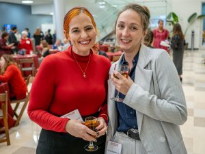 One woman in a red sweater and another in a gray blazer smile