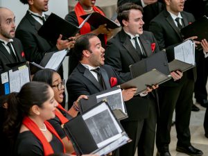 A few choir members with mouths open singing, holding sheet music