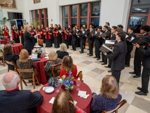A choir dressed in black is standing in front of tables with guests