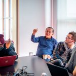"A professor gestures while speaking to a group of students."