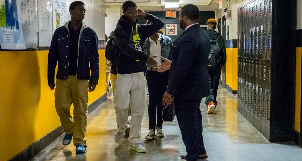 Photo of Mills greeting students in the hallway between classes.