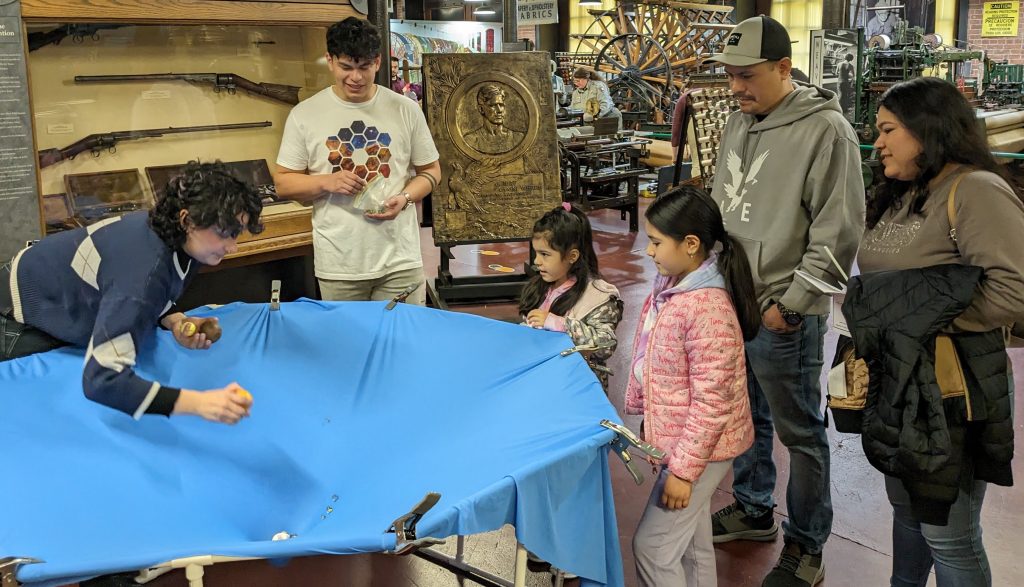 Stephanie Montoya and Renzo Herrera show visiting families and students their "spacetime spandex" demonstration of curved spacetime near the Sun, which deflects the path of nearby light rays. This effect is only viewable from Earth during a solar eclipse and helped confirm Einstein's theory.