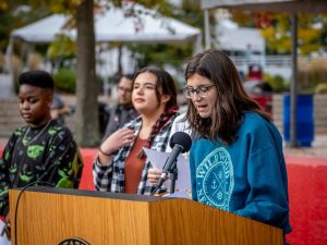 Student at microphone reading Land Acknowledgement with other students standing to her right
