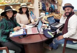 Three students wearing hats sitting at table discussing fashion merchandising