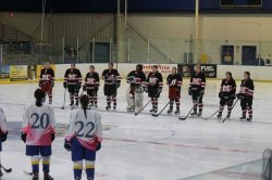 Nine people in a black hockey uniform, on an ice hockey field facing another line of hockey members