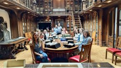 student Emily Walker sits at a long table in a library and archive room along with other workshop participants