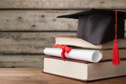 Image of a stack of books with a diploma and a graduation cap.
