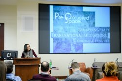 Image of Teresa Fiore lecturing at the podium with a book cover in the background.