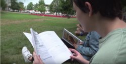 Image of high school student sitting on grass outside reading an Italian book