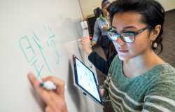 female student at whiteboard with tablet