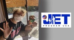 photo of Alumna Cara Roser waving at the camera. she is wearing a mask and holding a paintbrush. The JET teaching logo is on the right side of the image