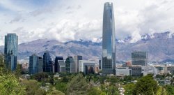 Photo of cityscape of Chile's capital city of Santiago. Tall buildings, trees, mountains and clouds