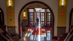 Student walking into Feliciano School of Business lobby backlit by sunrise