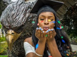 Montclair State University female student, wearing graduation cap, blowing confetti.