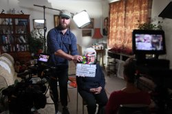 Justin Reddington McCarthy holds a director's clapboard while Eva Schloss sits on a chair behind him