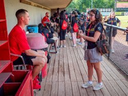 A student interviews a baseball player in a dugout.