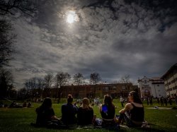Students watch the eclipse, while sitting on the grass.