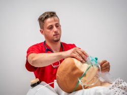 Male Nursing student observing as a mask is placed on a manikin.