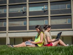 Two students sitting back to back outside of Blanton Hall in the grass.