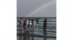 photo of people standing at waters edge with a horse and a rainbow in the background