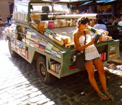 Photo of student reading and leaning against pick-up truck bookstore filled with books in Argentina.