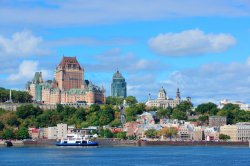 Quebec City skyline over river with blue sky and clouds.