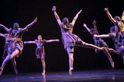 Photo of six dancers leaping toward a central point.
