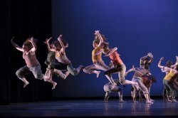 Photo of large group of dancers in formation and jumping.
