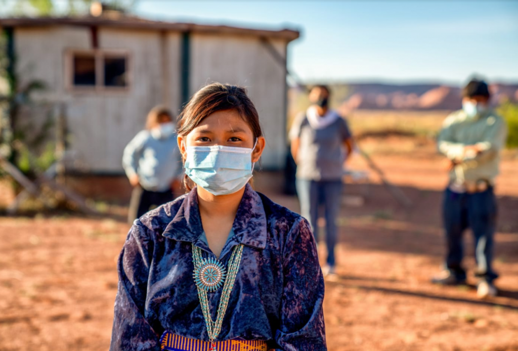 Young girl wearing Indigenous jewelry and accessories and a light blue disposable face mask on