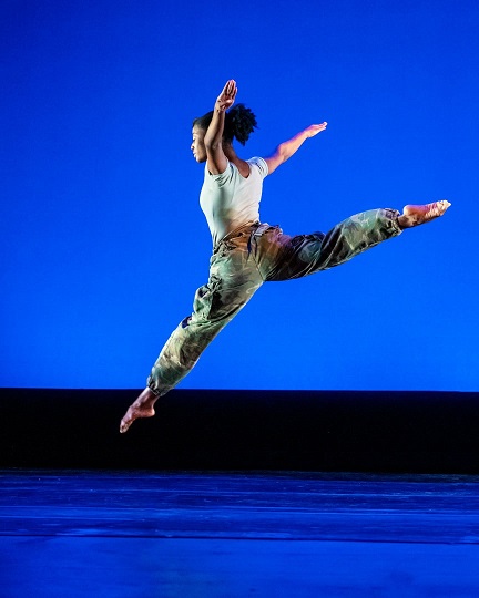 female dancer leaping on stage in front of blue background