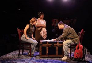three people sitting at table on stage acting