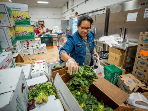 A woman picks up greens from a box.