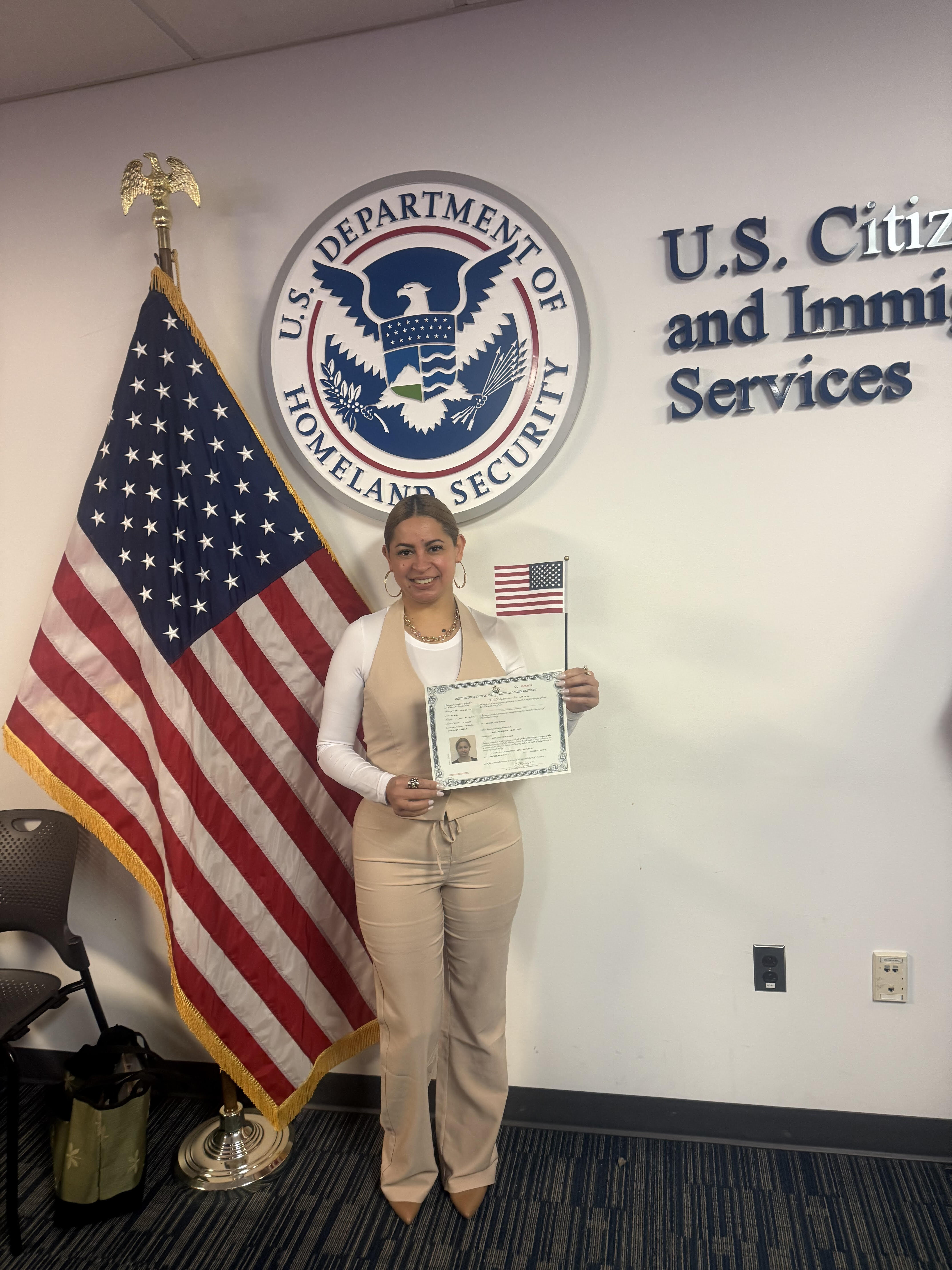 Maria Castillo holding up her Citizenship papers while smiling.