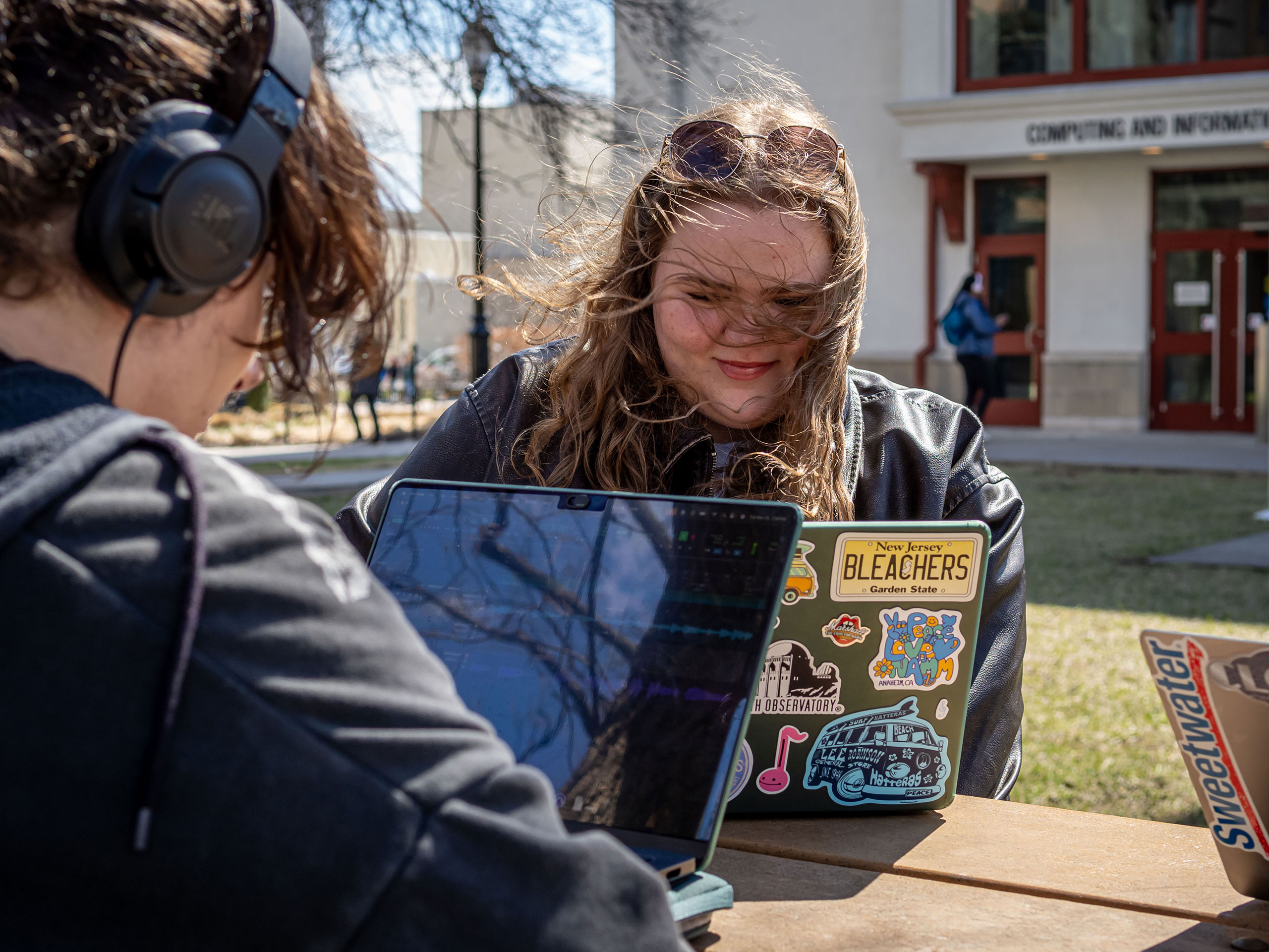 Two students working together on their laptops, outside, on a picnic table.