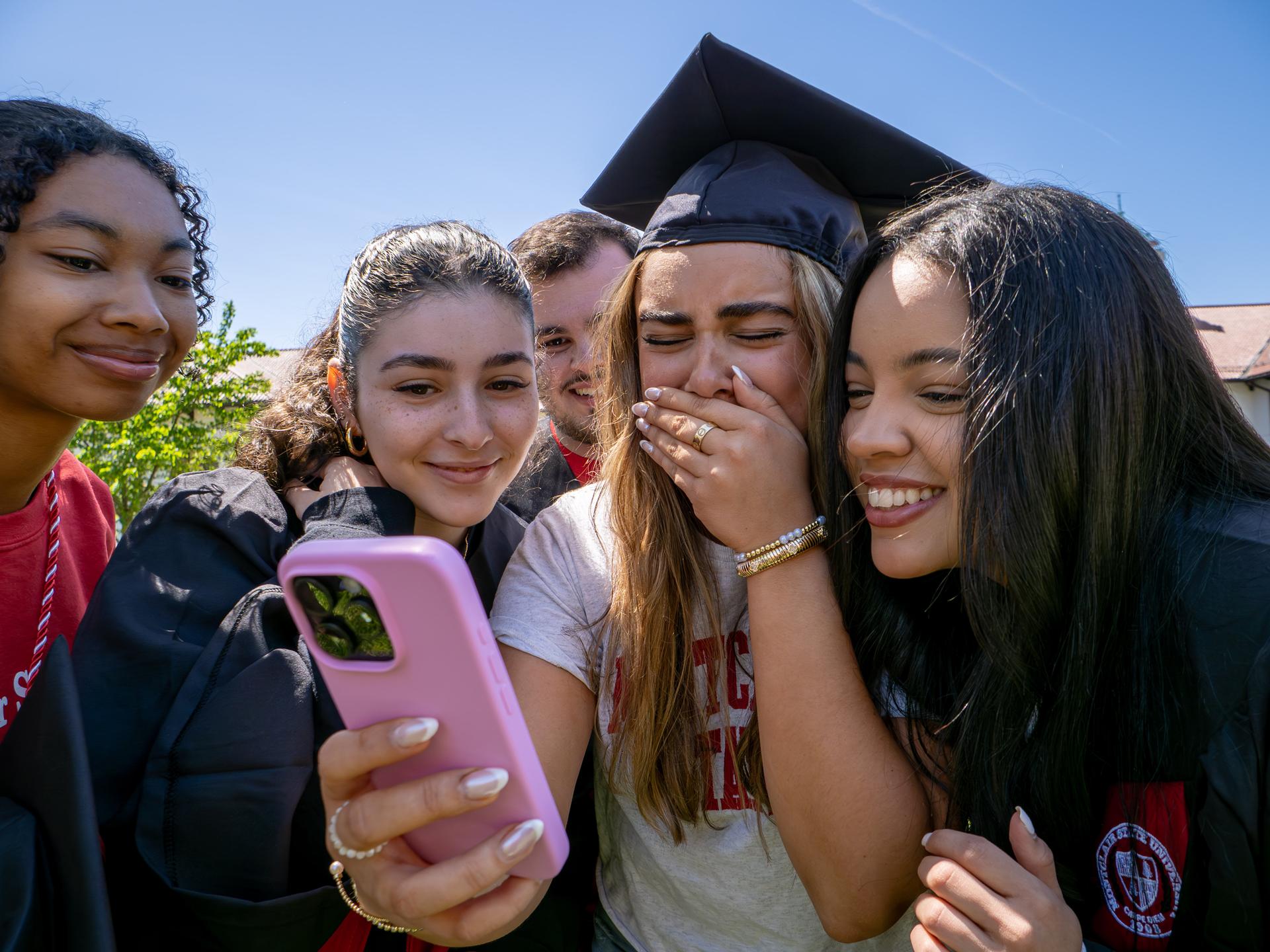 Group of five students looking at a phone.