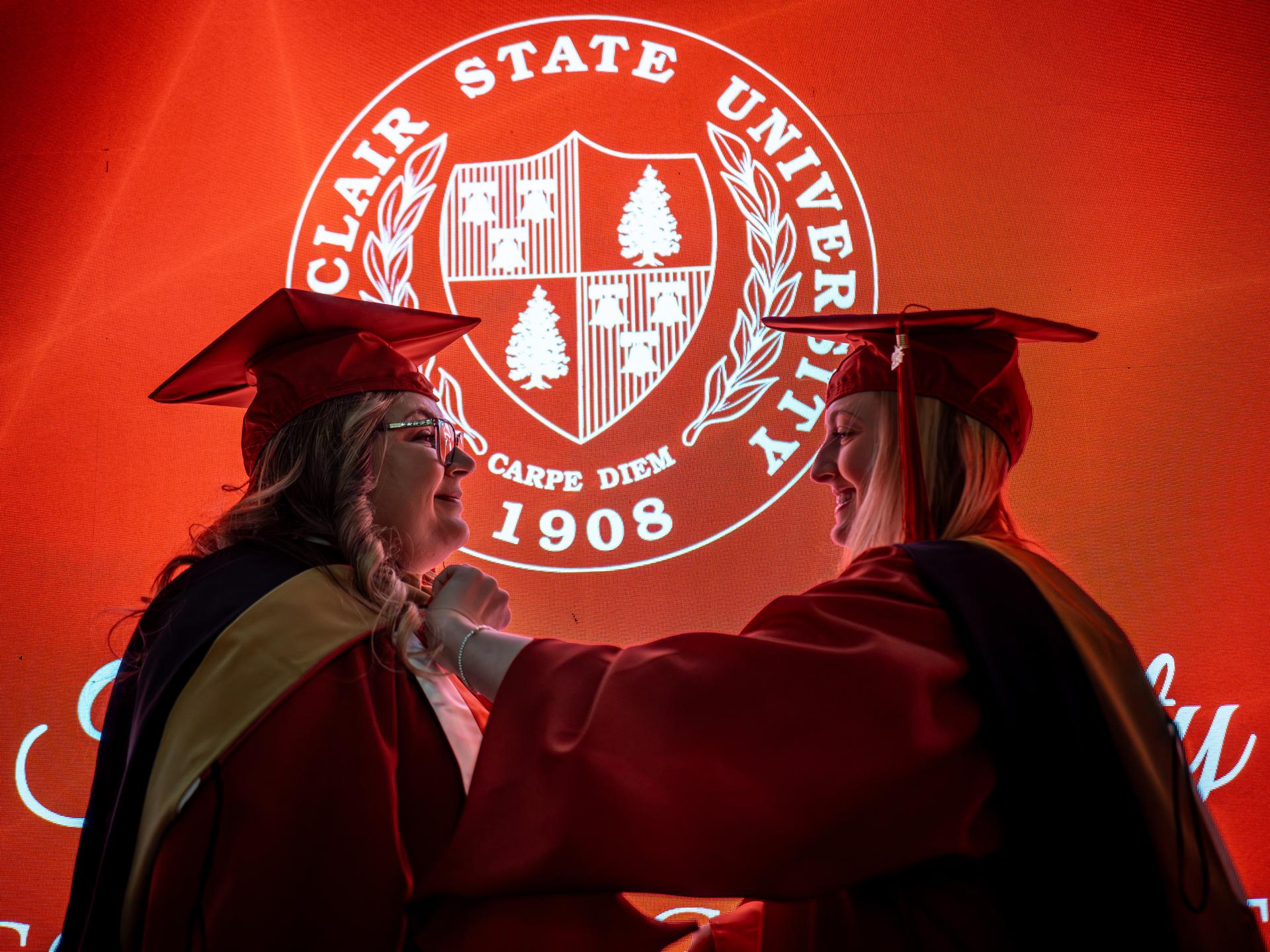 A photo of a woman fixing another woman's graduation attire at Winter Commencement