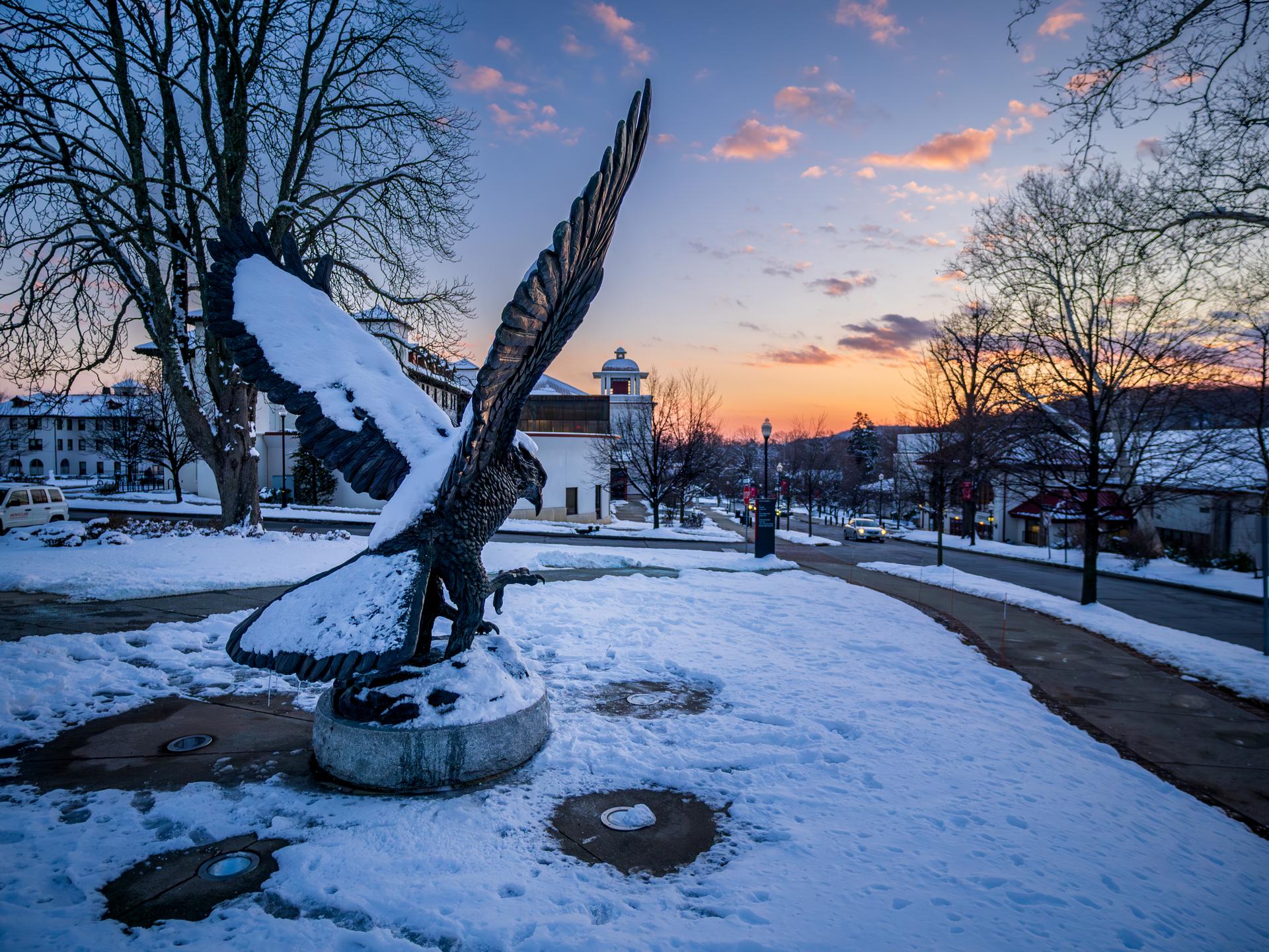 A photo of the snow covered red hawk statue on Montclair Campus at Sunset.
