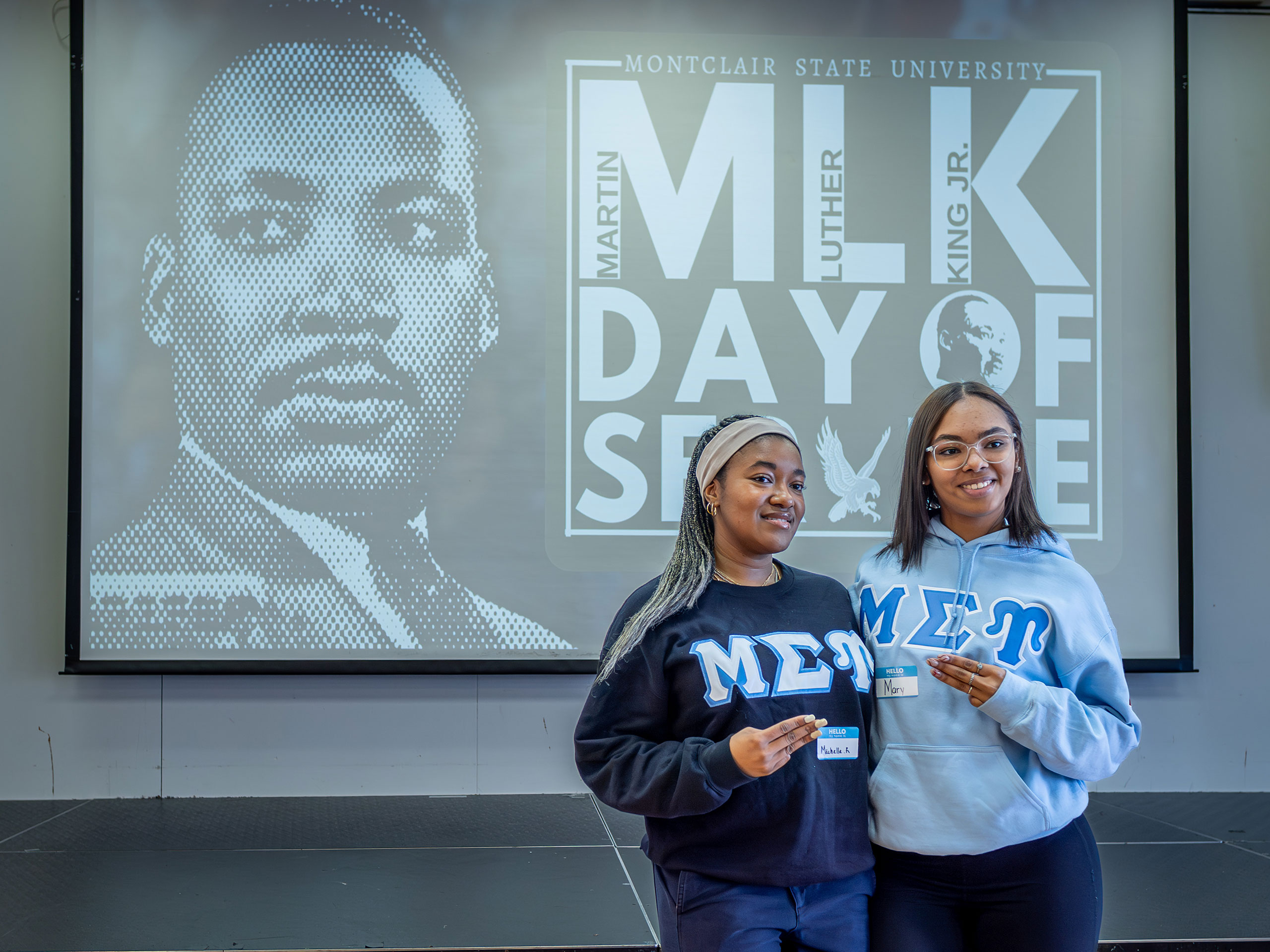 Two sorority members stand before a Martin Luther King Jr.’s Day of Service screen.