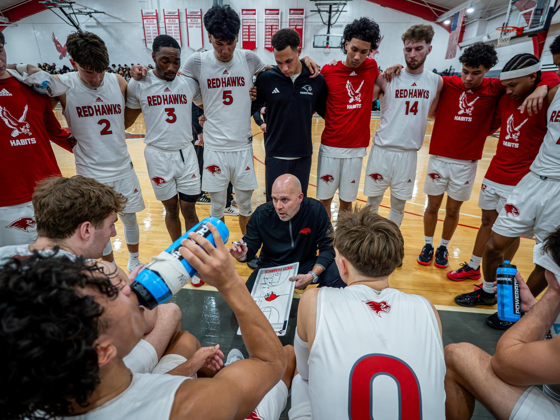 A photo of the Men's Basketball team and coach in a huddle