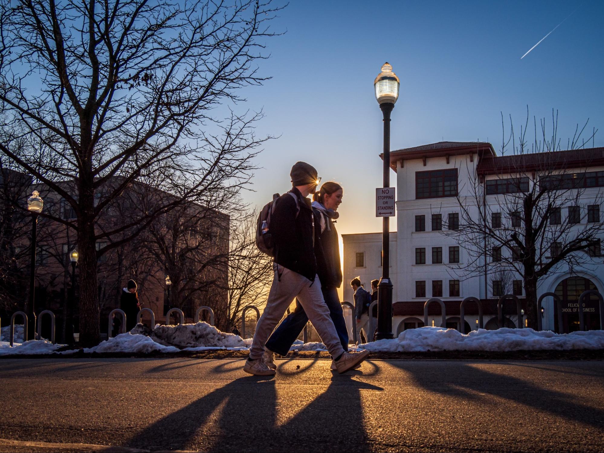 Two students walking in the campus with the sunset in the background.