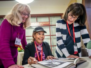Three ladies are smiling while looking at a yearbook.