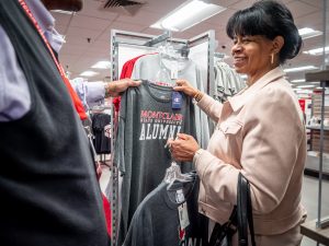 A woman holds up a gray shirt that says "Montclair Alumni" on it.