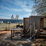 A plane flies over the Ironbound section of Newark, New Jersey, where industrial facilities dominate the landscape. Down Bottom Farms, a community garden built on raised beds sits on top of an industrial brownfield and offers a hopeful vision of a healthy future.